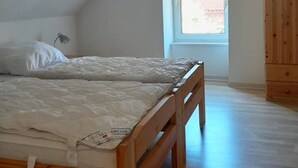 Een slaapkamer met twee houten bedden, een raam met uitzicht op een bakstenen gebouw en een houten garderobe.