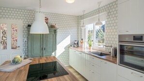 Une cuisine dotée d’un plan de travail en bois, de meubles blancs, d’un four encastré et d’une fenêtre laissant entrer la lumière naturelle.