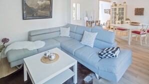 Un salon moderne avec un canapé d’angle bleu clair, une table basse blanche et un coin repas comprenant une table et des chaises blanches.