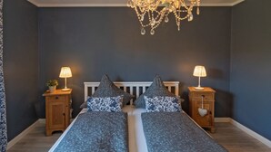 Un lit double avec une tête de lit blanche, deux tables de chevet avec des lampes et un lustre.