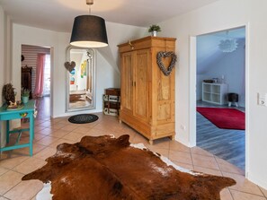 Ein geräumiges Wohnzimmer mit einem großen Kuhfellteppich, einem Holzkabinett mit Herzverziierung und einem Spiegel, der den Raum reflektiert.