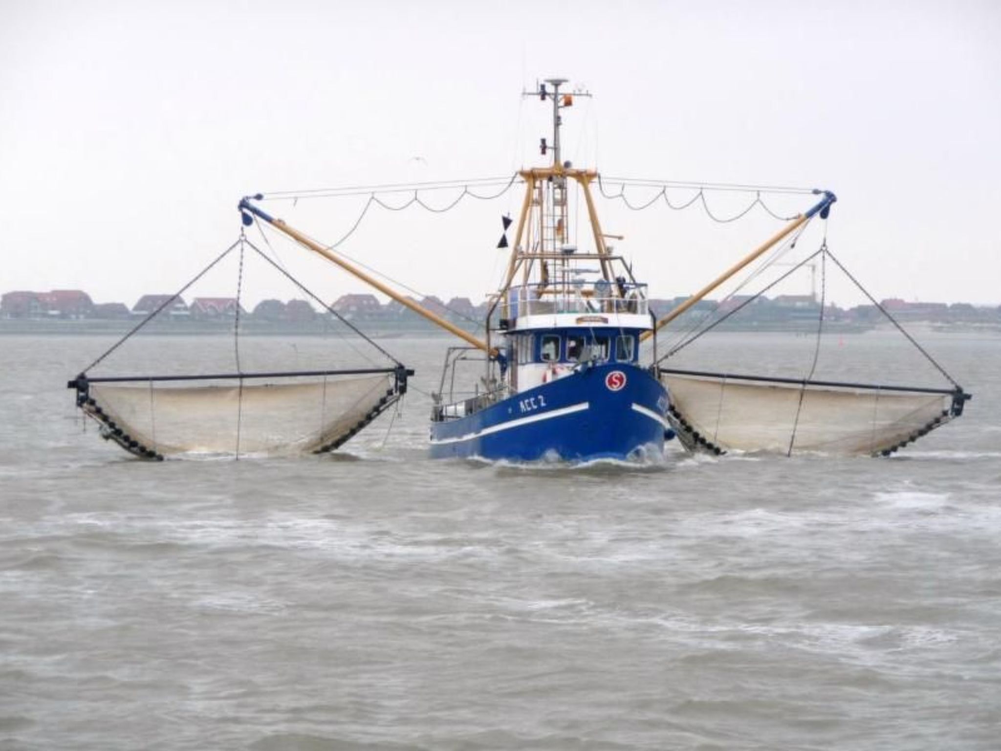 Un bateau de pêche, équipé de deux grands filets déployés, navigue sur une mer agitée.