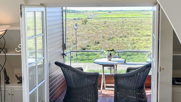Une pièce dotée d’une grande porte-fenêtre coulissante qui donne sur un patio extérieur aménagé avec des meubles en osier et une table.