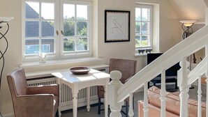 Un coin repas avec une table et des chaises, un tableau encadré au mur et un escalier en arrière-plan.