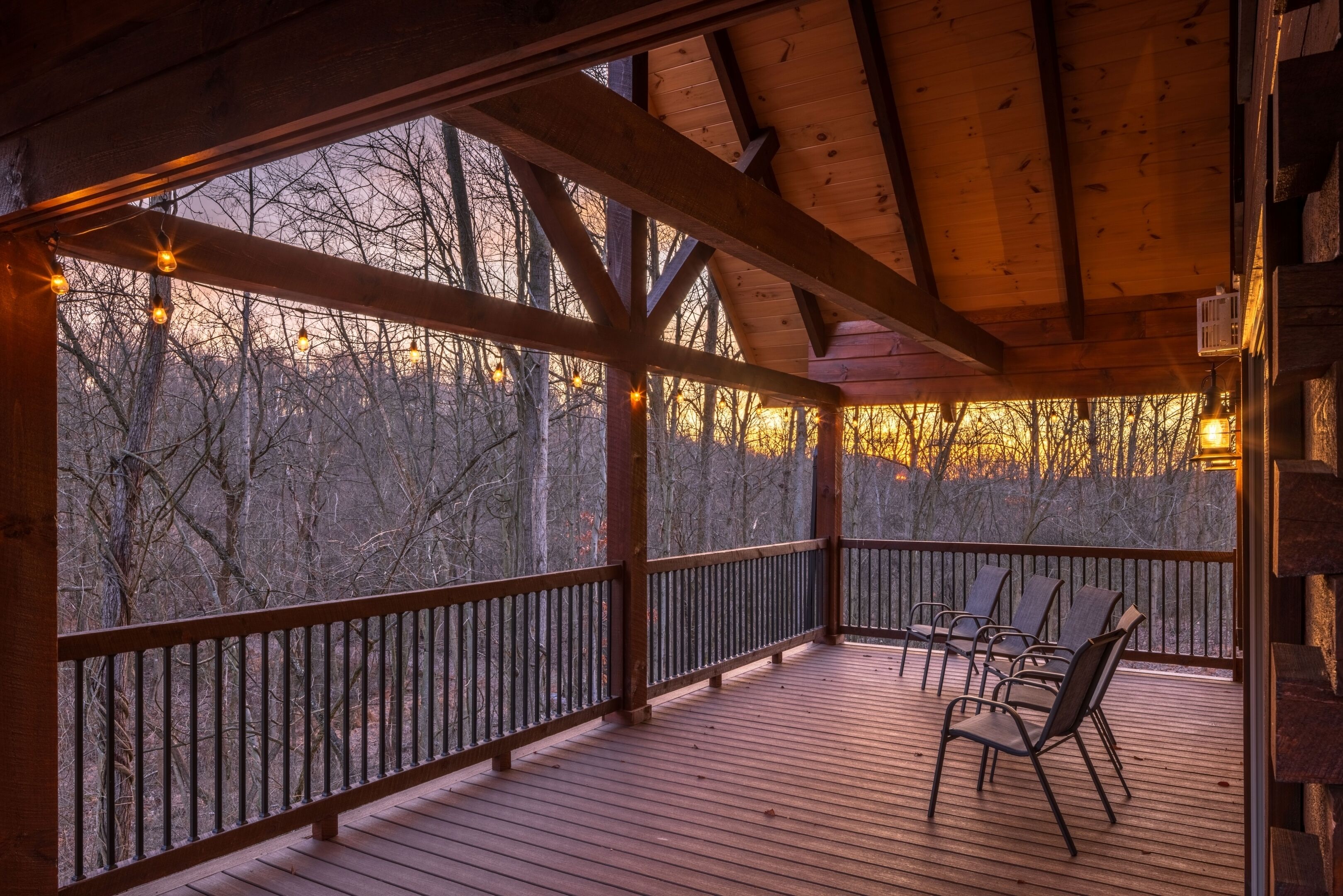 Une terrasse en bois, dotée de chaises et d’une rambarde, qui offre une vue sur une zone boisée.