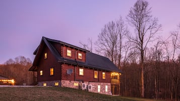Une grande cabane en rondins dotée de nombreuses fenêtres, d’une fondation en pierre et d’une antenne parabolique.