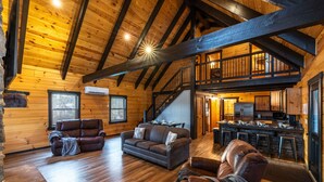 L’intérieur d’une cabane en rondins, avec un plafond en bois, un escalier, un salon doté de canapés en cuir et un coin cuisine.