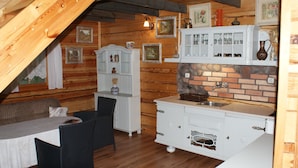 A cozy attic room with wooden beams, a dining table with chairs, a white cabinet with glass doors, and a brick backsplash. - Ruhe am Meer - Ferienhäuser in den Gärten von Magra by Interhome (Darlowo)