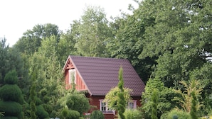 A red house with a sloped roof surrounded by well-maintained greenery and trees. - Ruhe am Meer - Ferienhäuser in den Gärten von Magra by Interhome (Darlowo)