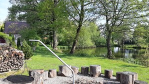 A rustic outdoor area with a grill, firewood, and a pond surrounded by trees. - Ruhe am Meer - Ferienhäuser in den Gärten von Magra by Interhome (Darlowo)