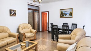 Una sala de estar con sofás de cuero, una mesa de centro de vidrio, una mesa de comedor con sillas, una araña y dos cuadros en las paredes.