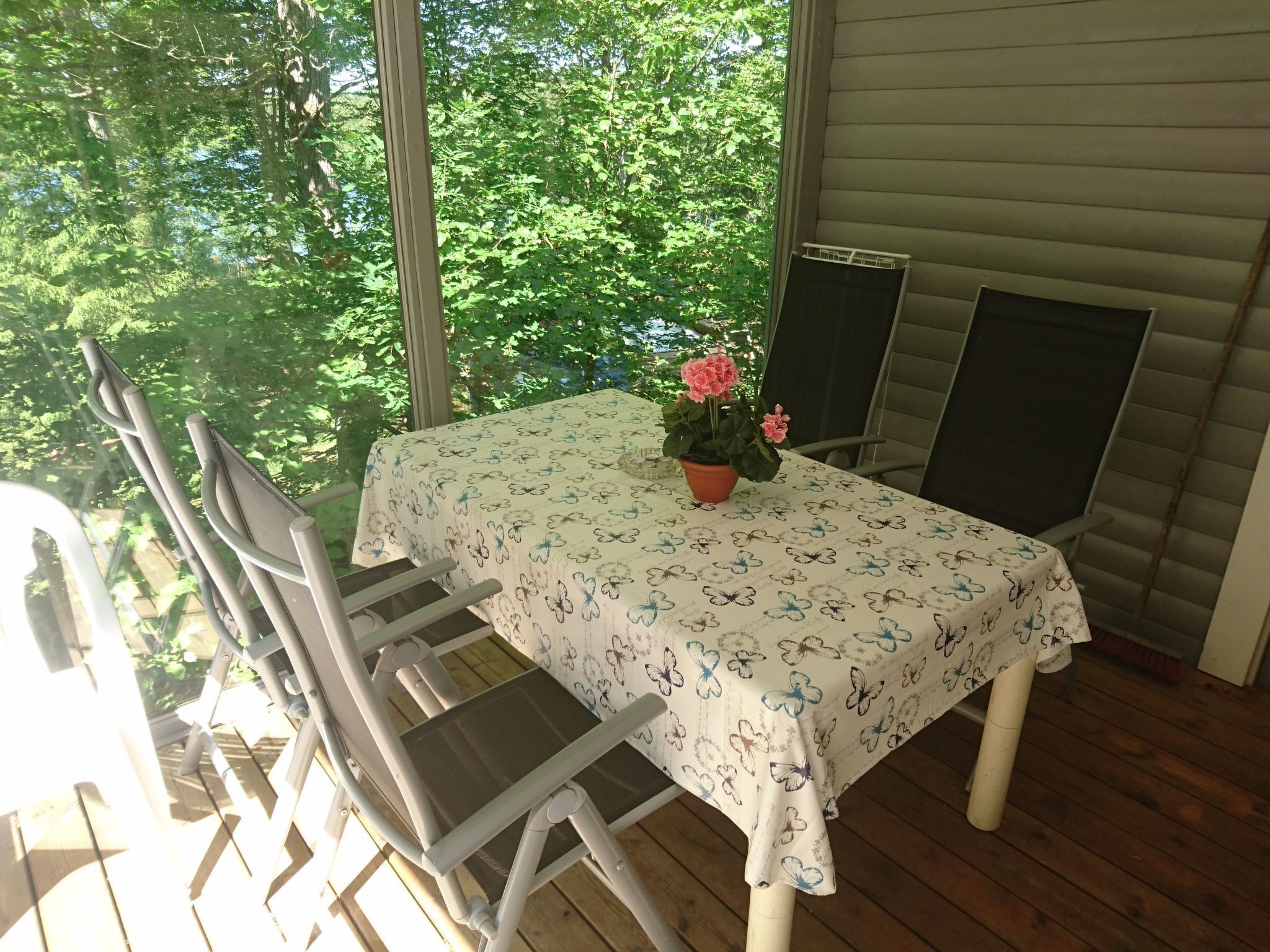 En täckt uteplats med ett bord och stolar, en krukväxt och utsikt över grönskan utanför.