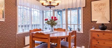 A dining area with a wooden table and chairs, a chandelier, and a window with a view of trees.