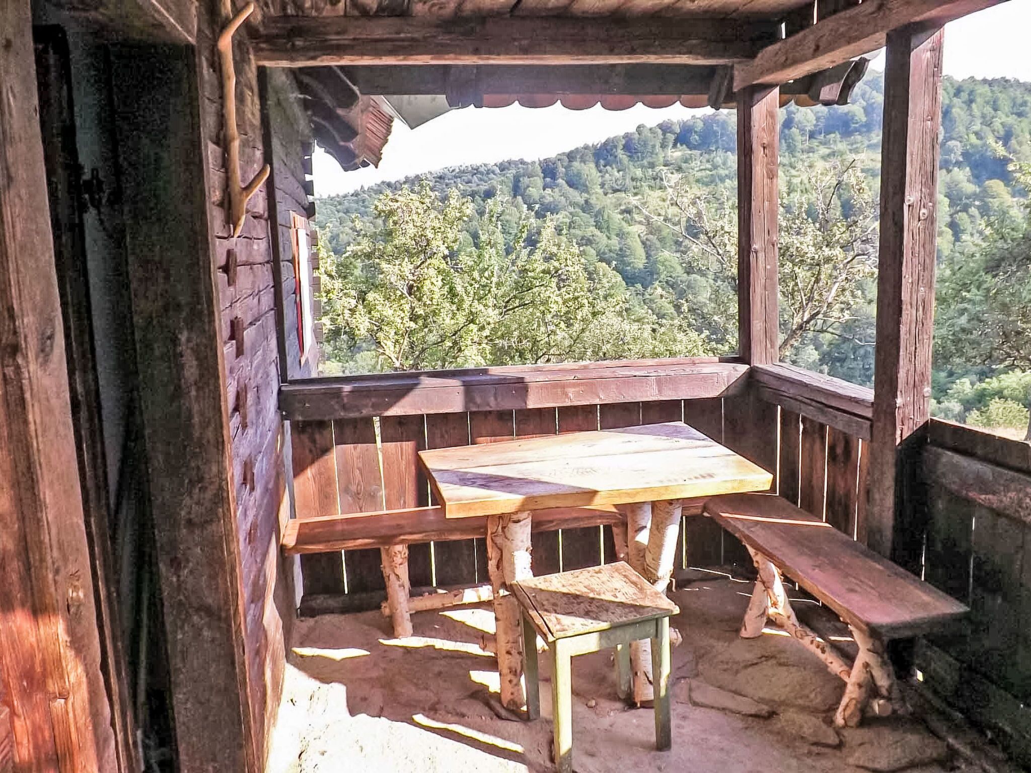 A wooden deck with a table and benches, overlooking a forested hillside.