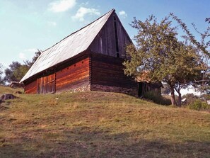 A rustic wooden barn with a sloped roof, situated on a grassy hill with trees in the background.