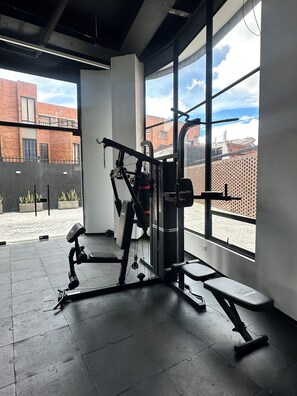 Ein Fitnessraum mit Trainingsgeräten, großen Fenstern und Blick auf Gebäude.