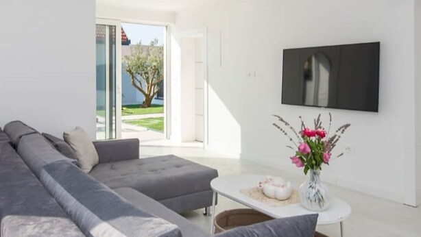 A modern living room with a grey sectional sofa, a white coffee table, and a flat-screen TV mounted on the wall. - "Luxury Grey house" by Interhome (Domanovići)