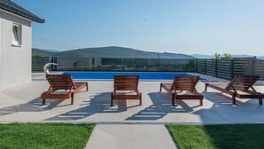 A rooftop pool area with wooden loungers and a clear view of mountains in the background. - "Luxury Grey house" by Interhome (Domanovići)