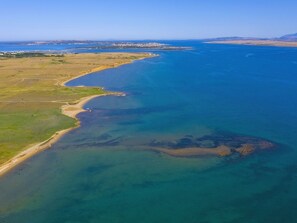 Luftaufnahme einer Küstenregion mit klarem, blauem Wasser, Sandstränden und Gebäuden in der Ferne.