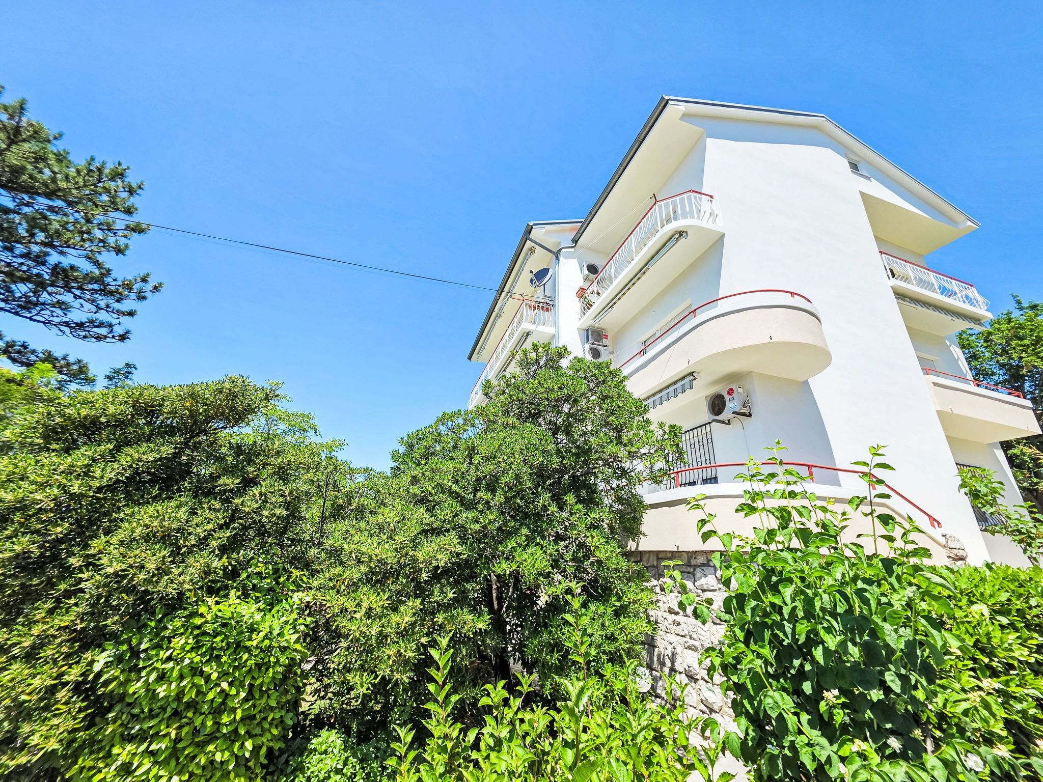 Un edificio de varios pisos con balcones, rodeado de abundante vegetación.