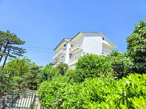 Un edificio de varios pisos con balcones, rodeado de abundante vegetación.
