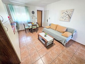 A living room with a sofa, a coffee table, a dining table with chairs, a kitchen area, and a door. - Appartement mit Balkon und Meerblick by Interhome (Crikvenica)