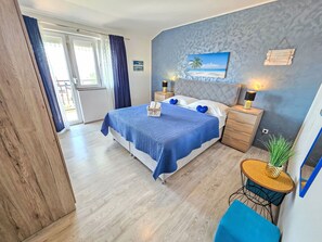 A bedroom with a bed, nightstands, a small table with a plant, and a view of the outdoors. - Appartement mit Balkon und Meerblick by Interhome (Crikvenica)