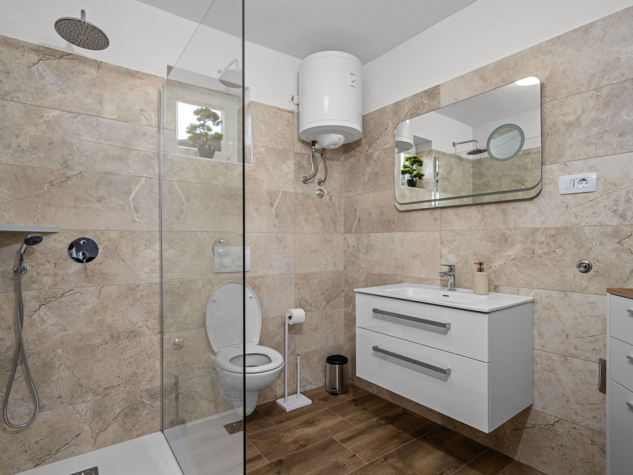 Een moderne badkamer met een glazen douchecabine, een toilet, een wastafel en een badmeubilair met lades.
