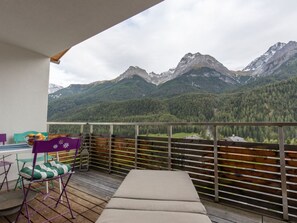 En balkon med udsigt til bjerge, et bord med stole og en polstret bænk.