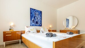 A modern bedroom with a wooden bed, two bedside tables with lamps, a large mirror, and a blue abstract painting on the wall. - Chasa Vista Lischana by Interhome (Scuol)