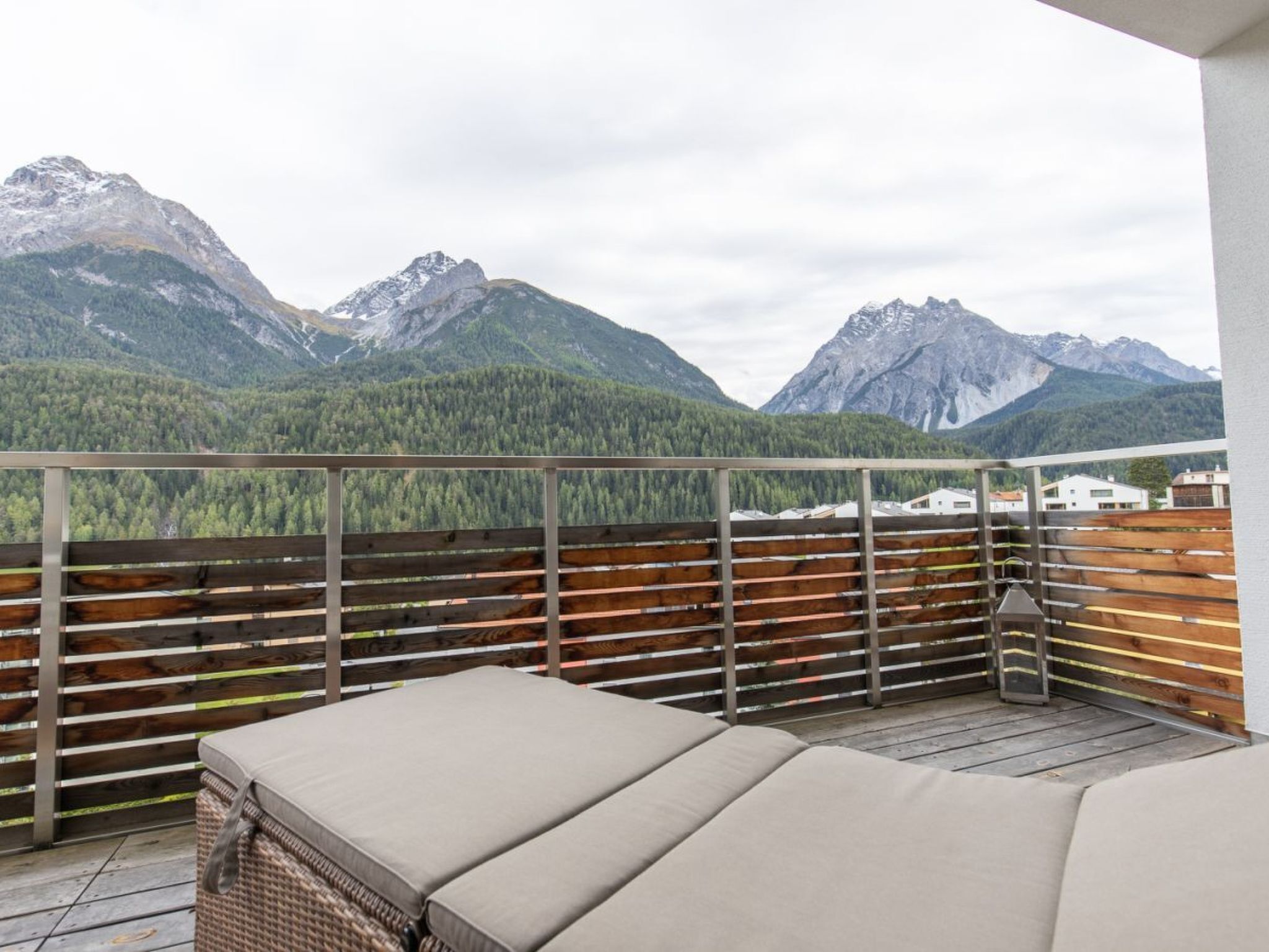 A balcony with a wooden railing, a wicker sofa, and a view of mountains.