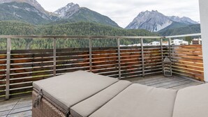 A balcony with a wooden railing, a wicker sofa, and a view of mountains. - Chasa Vista Lischana by Interhome (Scuol)