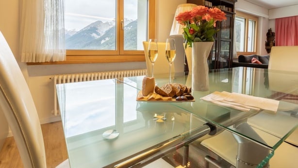 A modern room with a glass table, a view of mountains, a vase with flowers, and a bookshelf. - Chasa Vista Lischana by Interhome (Scuol)