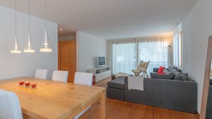 En moderne stue med et træspisebord, en grå sofa og et fjernsyn på et hvidt tv-bord.