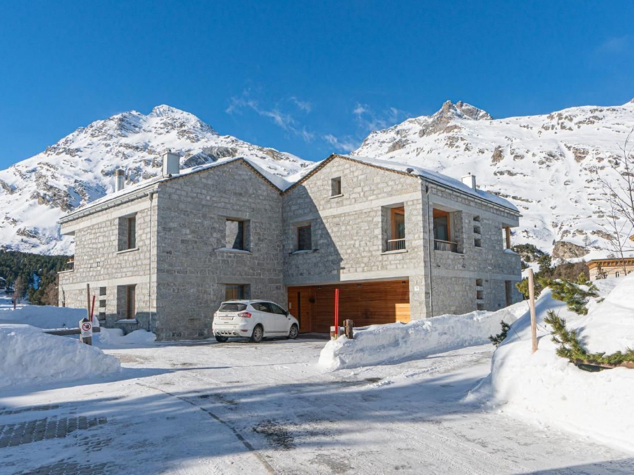 Un edificio de piedra con un coche estacionado frente a él, rodeado de nieve y montañas.