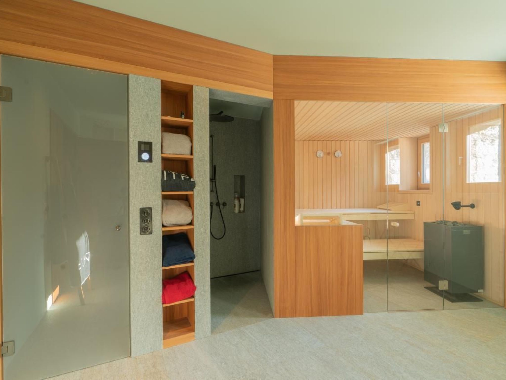 Un baño moderno con tocador de madera, zona de ducha y estantería empotrada con toallas.