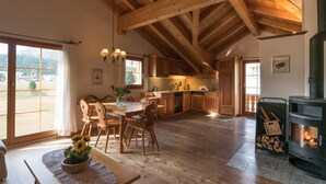 A spacious kitchen with wooden beams, a dining area with a table and chairs, and a wood-burning stove. - Chesa Trais FluorsC3 by Interhome (Maloja)