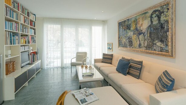 A modern living room with a white sofa, a coffee table, a bookshelf, and a large painting on the wall. - Residenz Alpenrose34 by Interhome (Sils Maria)