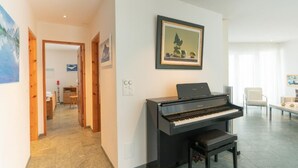A modern living room with a grand piano, a dining area, and a hallway leading to another room. - Residenz Alpenrose34 by Interhome (Sils Maria)