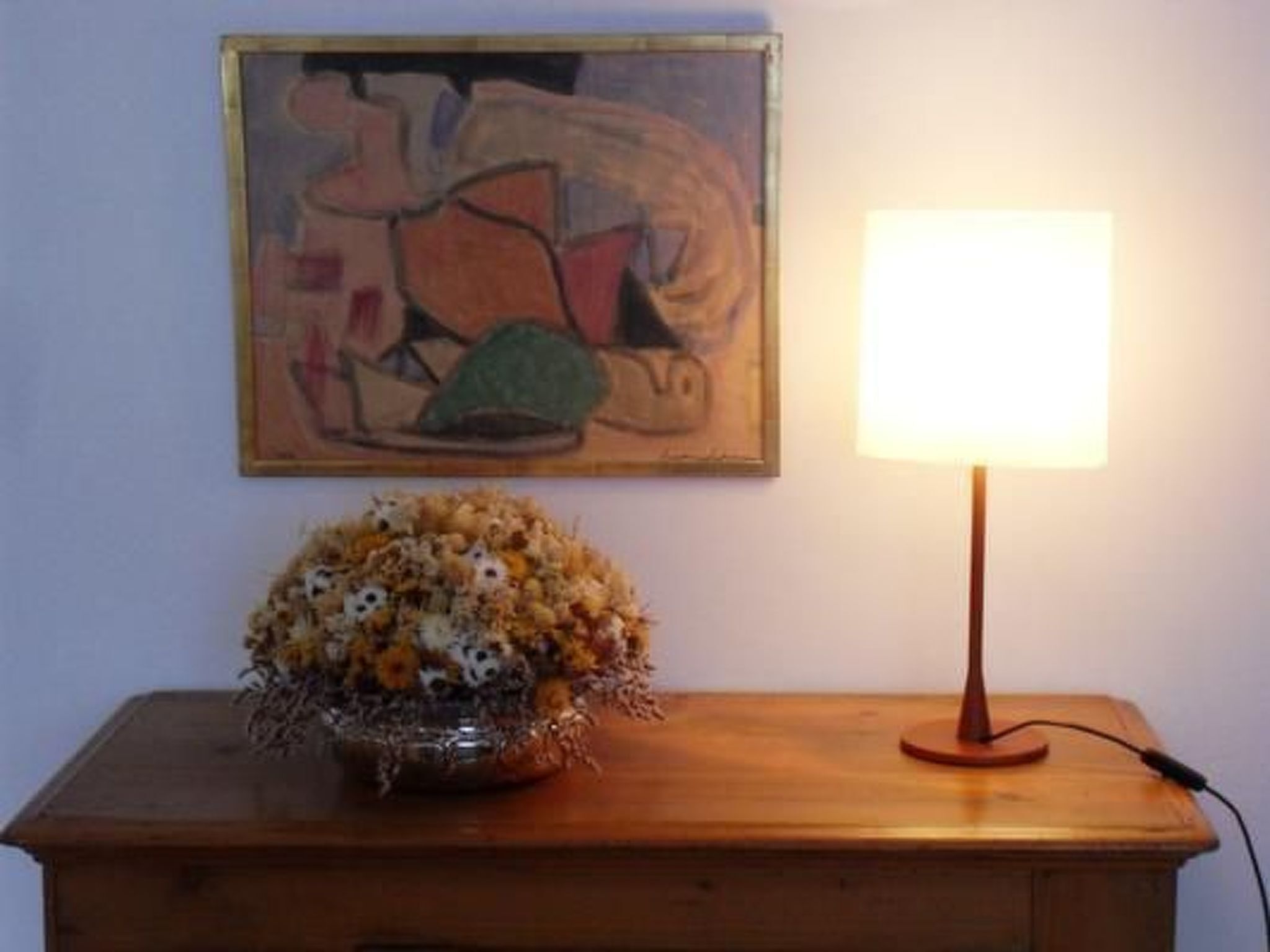 A wooden table with a lamp and a vase of flowers.