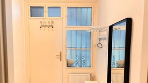 A small, bright room with a white door, a window with blinds, a radiator, and a mirror. - Charming Flat by Interhome (Vienna / 10. District)
