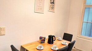 A dining area with a wooden table, four chairs, a black coffee maker, and a box of coffee. There are two framed pictures on the wall. - Charming Flat by Interhome (Vienna / 10. District)