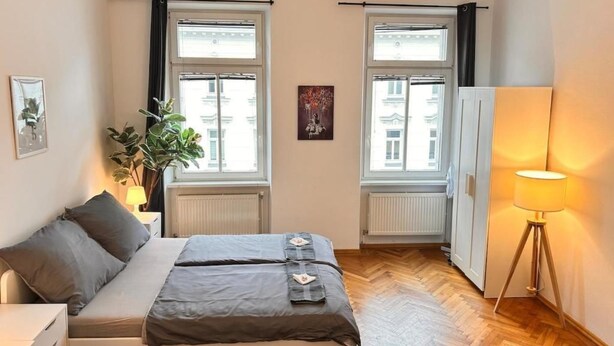 A bedroom with a bed, a desk, a lamp, and two windows with curtains. - Charming Flat by Interhome (Vienna / 10. District)