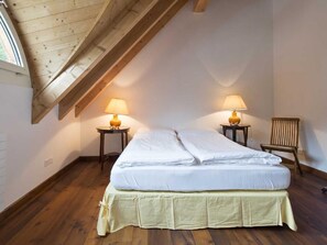 Une chambre avec un plafond en pente, deux tables de chevet avec des lampes, un lit avec une jupe verte et une chaise en bois.