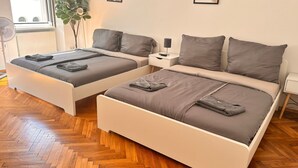 Camera doppia con due letti singoli, un comodino con lampada, un termosifone, una pianta in vaso e una finestra con vista sugli edifici.