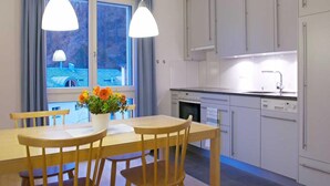 A modern kitchen with white cabinets, a dining table with chairs, and a window with curtains. - Residenz Alpenrose22 by Interhome (Sils Maria)