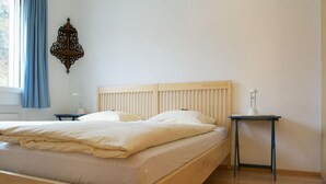 A wooden bed with a headboard, a bedside table, and a wall-mounted lamp. - Residenz Alpenrose22 by Interhome (Sils Maria)