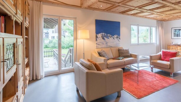Un salon spacieux avec une grande fenêtre, un tableau représentant des montagnes et un plafond en bois.