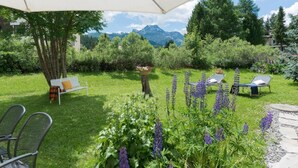 Un jardin agrémenté d’un banc, d’une table et d’un espace barbecue, le tout entouré d’une végétation luxuriante et de fleurs.