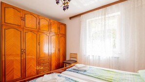 Hotellihuone, jossa on kaksi sänkyä, puinen vaatekaappi ja kattokruunu.